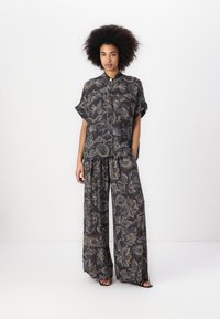 Schwarzes Blumenmuster-Outfit mit weit geschnittenen Hosen und einem kurzärmeligen, kragenlosen Button-Up-Hemd. Der Stoff hat ein strukturiertes, gemustertes Design.