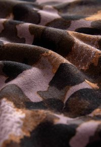Tessuto a motivi mimetici in tonalità di marrone, nero e lavanda; morbida texture con fibre visibili; drappeggiato in pieghe delicate, evidenziando le variazioni di colore.