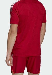 Czerwona koszulka sportowa i spodenki z geometrycznym wzorem, białe paski na ramionach oraz boczne rozcięcia dla wentylacji. Lekki, oddychający materiał.