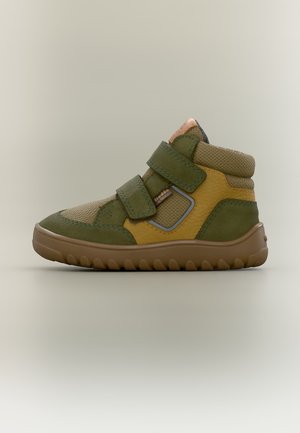 Basket montante pour enfant en vert et jaune avec deux bandes Velcro et une semelle marron texturée sur fond neutre.