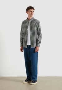 Camicia a quadri grigia e bianca con una maglietta bianca sotto, abbinata a jeans blu e sneakers blu navy.