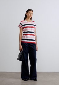 Ριγέ κοντομάνικη μπλούζα σε αποχρώσεις ροζ, κόκκινο και μαύρο, συνδυασμένη με σκούρα τζιν παντελόνια με φαρδιά μπατζάκια και μικρή μαύρη τσάντα. Λείο ύφασμα και χαλαρή εφαρμογή.