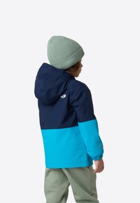 Jachetă ușoară, rezistentă la apă, în nuanțe de bleumarin și albastru deschis, cu glugă și manșete elastice, asortată cu o căciulă ribbină verde mentă.