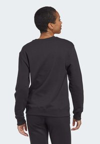 Černá mikina s dlouhými rukávy, kulatým výstřihem a volným střihem, s žebrovanými manžetami a pasem, na světlém šedém pozadí.