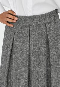 Pelēka plisēta svārku izgatavota no teksturēta auduma. Ar pieguļošu jostu un smalkiem krāsas variantiem, piemērota dažādiem apģērba komplektiem.