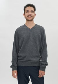 Grau, leichter V-Ausschnitt-Pullover mit langen Ärmeln und gerippten Bündchen, aus weichem Stoff, kombiniert mit dunkler Hose.