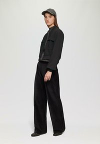 Czarna krótka kurtka z dwoma przednimi kieszeniami, zestawiona z szerokimi czarnymi spodniami z korduroju. Model nosi szary czapkę i błyszczącą bluzkę pod spodem.