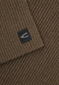 Bruin geribbeld breigoed met een zwart vierkant label en een grijze logo-accent. Getextureerd oppervlak met zichtbare vezels voor warmte.