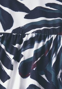 Tkanina w kwiatowy wzór z ciemnoniebieskimi i turkusowymi wirami na białym tle, z marszczonym szwem dla dodatkowej tekstury.