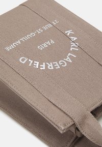 Beige stoffen portemonnee met een gestructureerd oppervlak, voorzien van reliëf zilveren tekst. Het ontwerp heeft een klep-sluiting en zichtbare stiksel details.