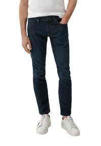 Donkerblauwe denim jeans met een slim fit, met vijf zakken en subtiele stikseldetails. Gecombineerd met witte lage sneakers.