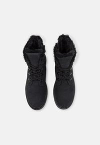 Bottes noires pour cheville avec doublure en fausse fourrure, design à lacets, bout arrondi et tissu texturé. Dotées d'œillets métalliques pour les lacets et de détails de couture.