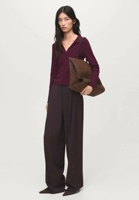 Pull marin à col en V associé à un pantalon palazzo noir. Tenant un sac à main en daim marron au design plié unique et avec des contours contrastants.