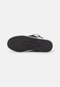 Black rubber shoe sole with textured pattern, featuring a circular logo and raised accents; reinforced tread for grip and durability.