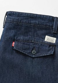 Tummansiniset farkut, joissa on napillinen takatasku, Levi'sin punainen lippu ja valkoinen Levi Strauss -merkki lähellä vyötäröä.