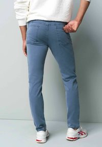 Jeans slim fit bleus avec une texture lisse, un design cinq poches et des détails de couture visibles. Associés à des chaussures de sport blanches.