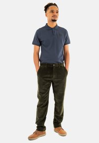 Polo shirt texturé bleu marine, pantalon en velours côtelé vert olive et chaussures marron clair. Tenue décontractée avec une coupe ajustée et des accents de boutons.
