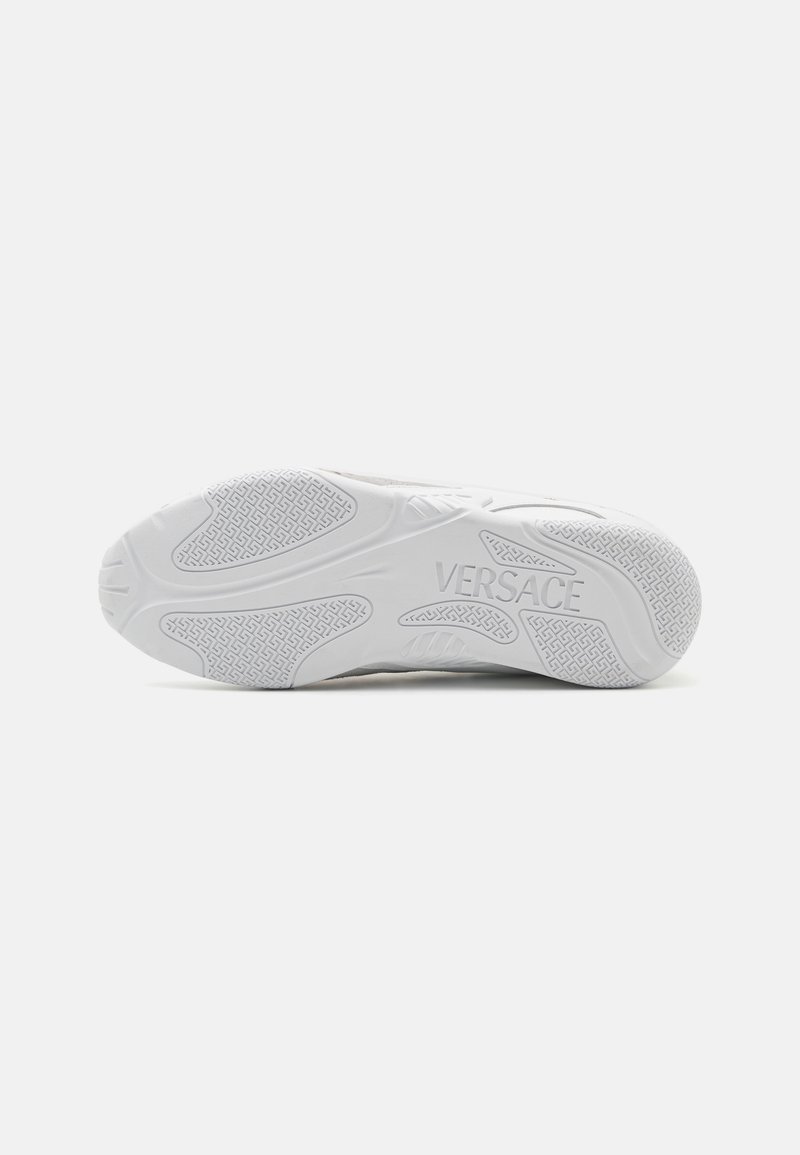 White sneaker sole featuring textured rubber, intricate tread pattern, and "VERSACE" logo embossed on the side.