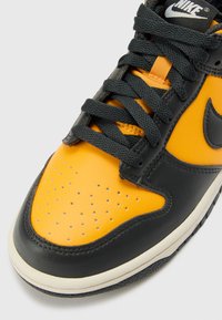 Nike Dunk Sneaker mit einer gelben Lederzehenkappe, schwarzen Lederseiten und grauen Schnürsenkeln. Verfügt über Belüftungsöffnungen an der Zehe und eine Gummisohle.