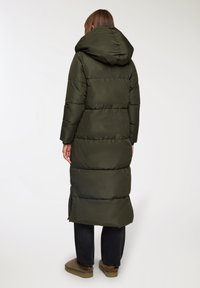 Cappotto cappotto lungo verde oliva con cappuccio, caratterizzato da pannelli trapuntati, una cerniera sul fondo e una texture di tessuto liscia e lucida.