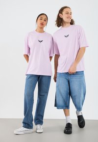 Light purple oversized t-shirts with a black butterfly graphic at the center, paired with blue denim jeans and casual shoes.