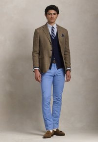 Καφέ καρό σακάκι πάνω από γαλάζιο γιλέκο, λευκό πουκάμισο με μπλε ρίγες, ανοιχτό γαλάζιο παντελόνι και καφέ μοκασίνια με υφή.