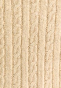Sweter z dzianiny w jasnym beżu, z pionowymi splotami z teksturowanym wzorem plecionym, prezentujący miękki, podobny do wełny materiał.