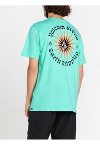 Turkusowa bawełniana koszulka z krótkim rękawem, z grafiką słonecznego promieniowania w kolorze czarnym i pomarańczowym, z tekstem "Volcom Store" oraz "Earth tripping".