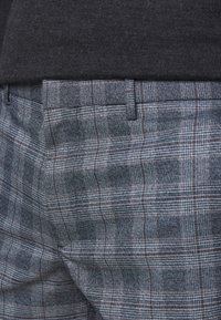 Herrarnas grå rutiga byxor med en texturerad tyg. Mönstret har korsande linjer i ljusa och mörka nyanser med subtila detaljer.