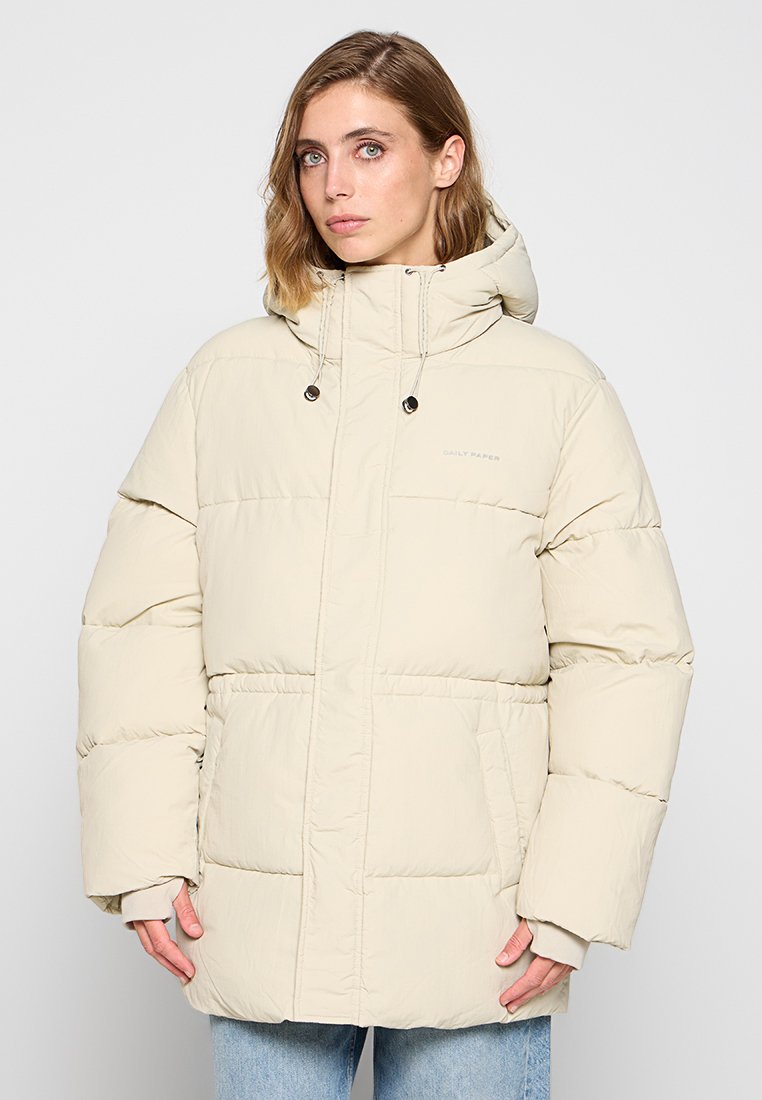Helle beige Steppjacke mit Kapuze, mit einem Reißverschluss vorne, großen aufgesetzten Taschen und einer gesteppte Textur. Logo auf der Brust gestickt.