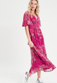Robe maxi fuchsia à fleurs avec un décolleté en V profond, des manches courtes flottantes et une taille cintrée. Assortie à des baskets multicolores. Tissu lisse.