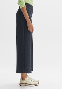 Pantalon large taille haute bleu foncé en tissu texturé, associé à des chaussures de sport légères présentant un mélange de couleurs.