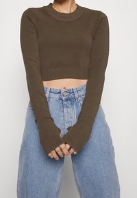 Ruskea lyhyt, pitkähihainen yläosa, jossa pyöreä pääntie ja resorireunus, yhdistetty korkeavyötäröisiin vaaleansinisiin farkkuihin.