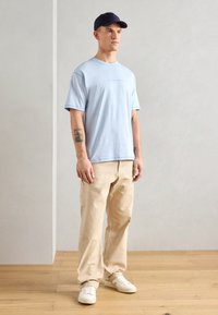 Světle modré bavlněné tričko s krátkým rukávem, v kombinaci s béžovými cargo kalhotami. Bílé tenisky a námořnická čepice doplňují outfitu.