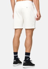 Hvide bomulds shorts med en baglomme, snoreliv og slim fit. Båret med sorte sneakers og mørke sokker med hvide striber.