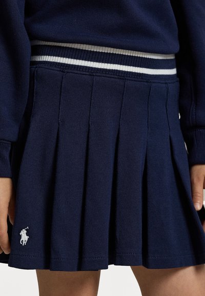Marineblå plissert skjørt laget av ribbet stoff, med en stripete midje med grå og hvite detaljer samt en liten brodert logo på kanten.