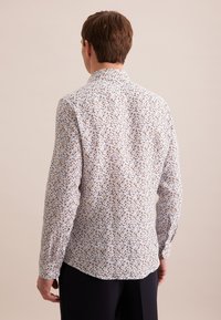 Langemouwig shirt van witte stof met een bloemenpatroon in blauwe, bruine en gele tinten; heeft een button-down kraag en een ronde zoom.