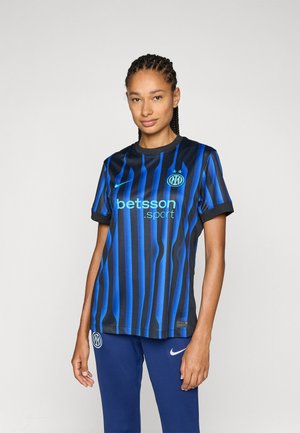 Svart og blåstripet fotballdrakt med kort erme, med rund hals, logo og sponsortekst i turkis. Stylet med blå bukser.