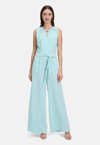 Mintgrön ärmlös jumpsuit med volangkrage, nyckelhålsutskärning och bälte i midjan, med vida byxben och slät tygtextur.