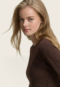 Pull en tricot marron avec un col rond et des manches longues, présentant une finition texturée et un subtil éclat sur un fond clair.