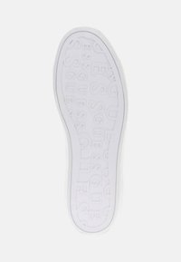 Sole di sneaker bianca con lettering testurizzato, con la scritta 'ESSGUES' in rilievo in diverse dimensioni e orientamenti su tutta la superficie.