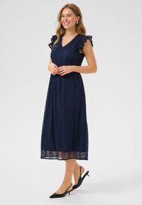 Marinblå spets midi-klänning med V-ringning, volangärm och diamantmönster samt genomskinlig nederkant; matchad med svarta slingback-klackar.