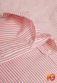 Chemise à rayures rouges et blanches avec un col à bouton. Tissu en coton lisse avec des rayures fines régulièrement espacées et patte de boutonnage dissimulée.