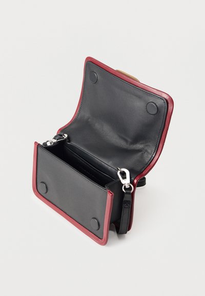 Μικρό ανοιχτό μαύρο δερμάτινο τσαντάκι με κόκκινο περιθώριο, ασημένια κλείστρα και αποσπώμενο λουρί σε λευκό φόντο.