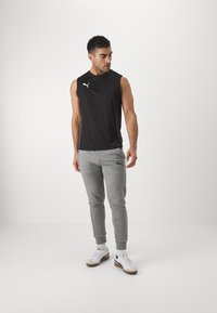 Zwarte mouwloze sportshirt met PUMA-logo, gecombineerd met grijze taps toelopende joggers met logo-accenten. Sneakers maken de look compleet.