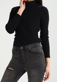 Svart ribbad polotröja med långa ärmar, åtsittande design. Matchad med mörkgrå slitna skinny-jeans med knäskärningar.