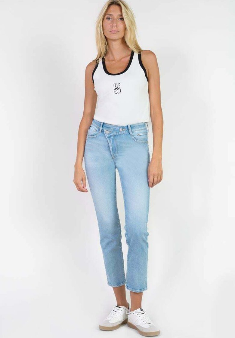 Un débardeur blanc avec des bords noirs et un logo, associé à un jean taille haute bleu clair et des baskets blanches. Texture en denim lisse.