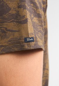 Bruin en gouden gestreepte stof met een textuurafwerking, voorzien van een klein blauw label gestikt aan de zoom.