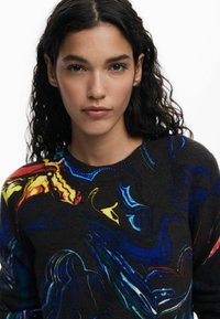Pull en tricot avec un fond sombre et des motifs abstraits colorés en rouge, jaune, bleu et vert. Col rond avec un tissu texturé.
