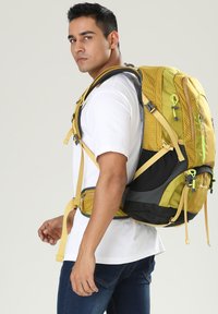 Sac à dos jaune et noir avec un motif en grille, des bretelles rembourrées, plusieurs poches et des accents verts lumineux. Tissu texturé et bretelles réglables.
